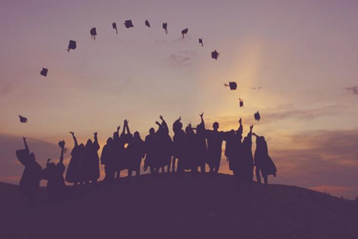 silhouetted graduates throwing their caps in the air