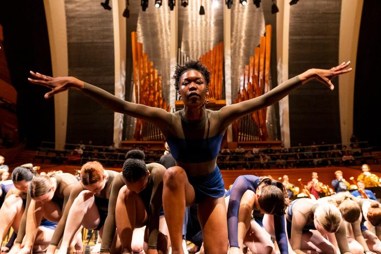 dancer spreads arms above other dancers bowing