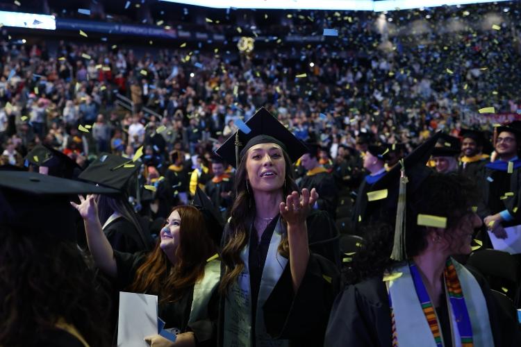 A graduate holds a hand out to catch confetti as it falls from the sky