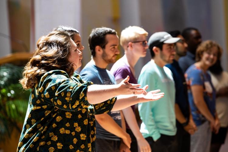 Roslinde Rivera stands in a row of singers with her arms reached out in front of her. 