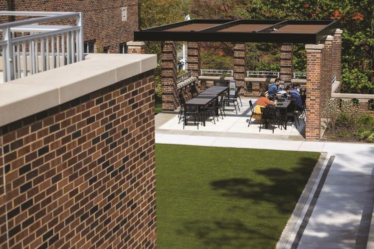 Students sit at an outdoor table in a covered area on the Bloch Terrace