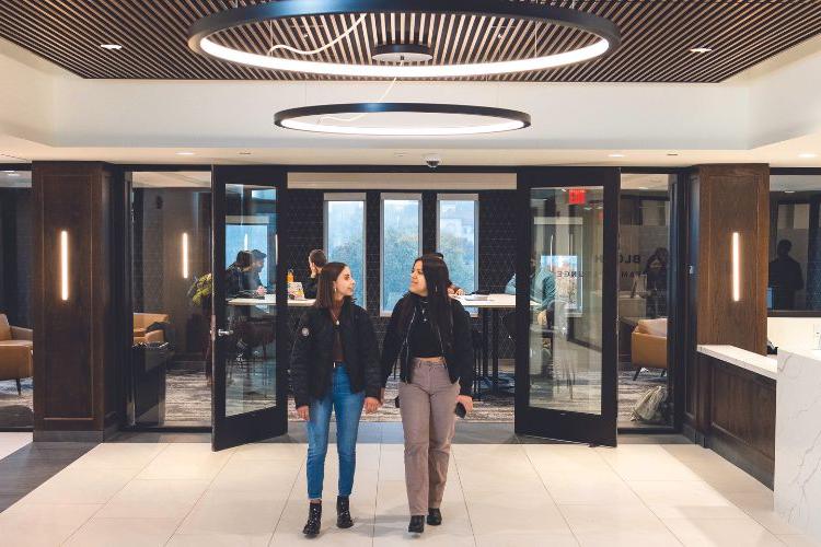 Two 学生 walk in the front door of Bloch Heritage Hall, into a bright, airy atrium