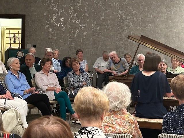 Beth plays the piano, 周围都是克拉里奇法院的居民，他们坐在椅子上倾听