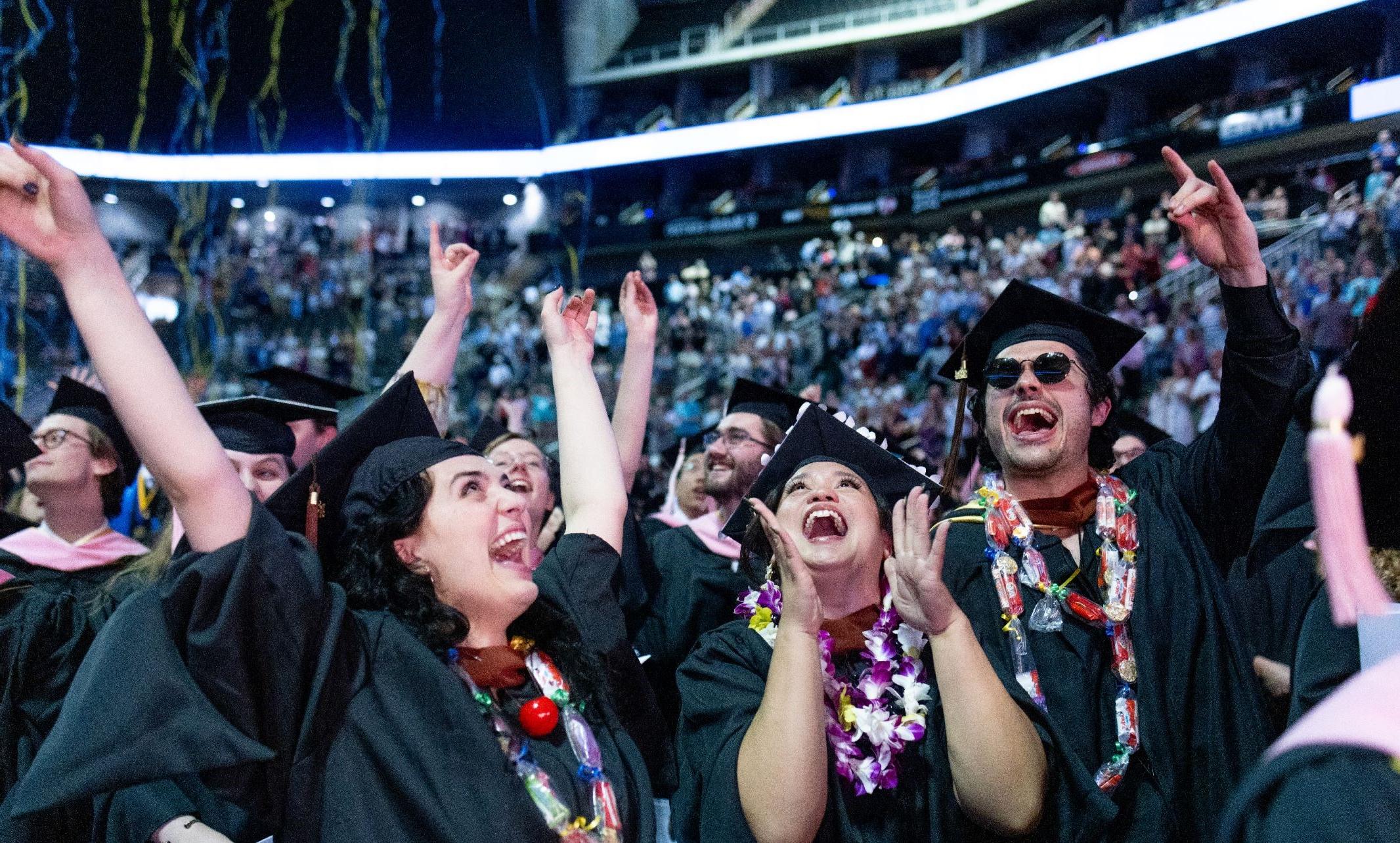 Graduates cheer and clap as streamers come down from the ceiling after commencement ceremony
