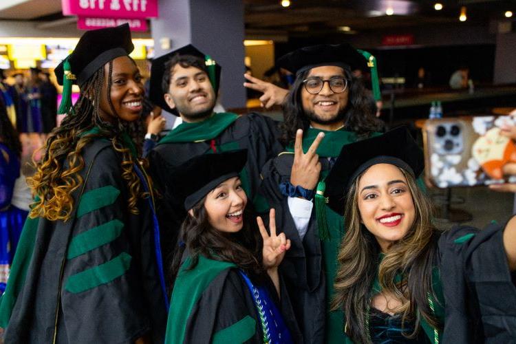 Five graduates from School of Medicine pose for a selfie wearing their regalia